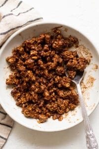 Granola in a white bowl with a spoon.