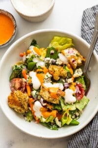 A white bowl with a salad and dressing on it.