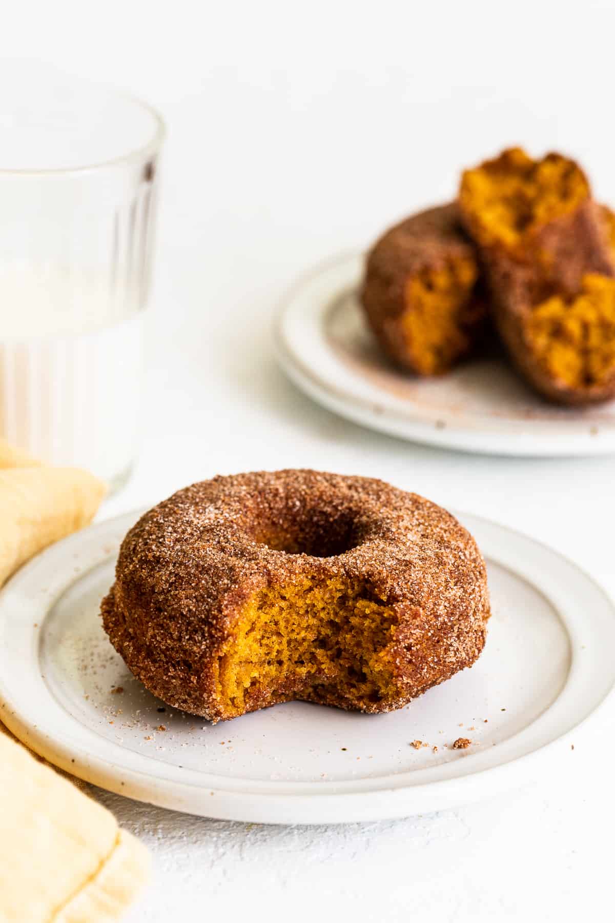 These baked pumpkin donuts are made with real pumpkin and a delicious cinnamon sugar topping. Plus, there's no frying involved! bite taken out of pumpkin donut on plate.