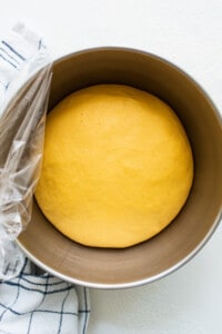 A yellow dough in a bowl with a towel on top.