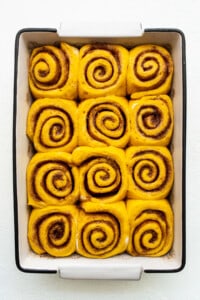 Cinnamon rolls in a baking dish on a white surface.
