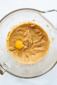A bowl of peanut butter with an egg in it.