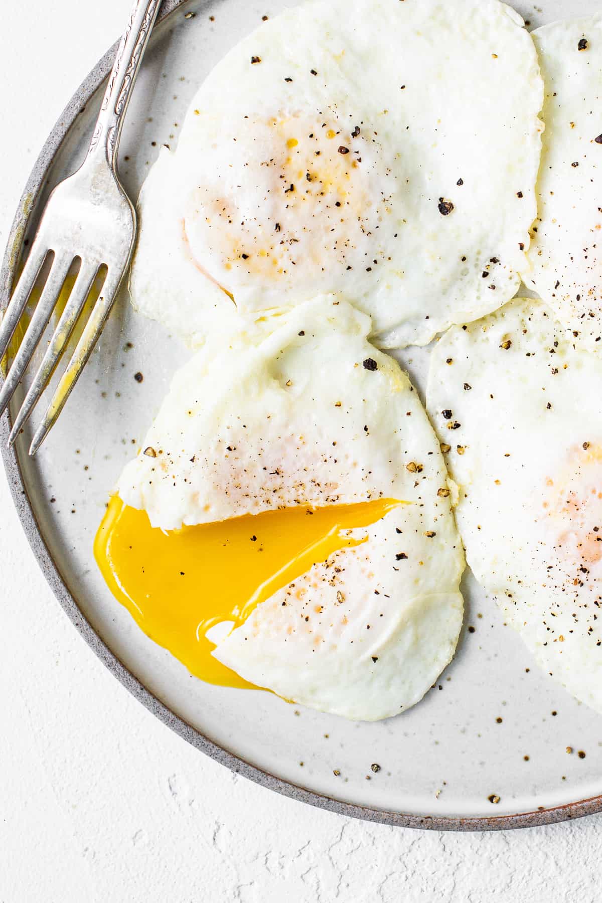 Over easy eggs on a plate with a fork.