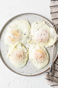 Four fried eggs on a plate with a napkin.