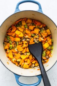 A pot filled with vegetables and turkey wild rice soup, alongside a black spatula.