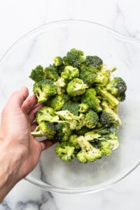 A person holding broccoli in a glass bowl.