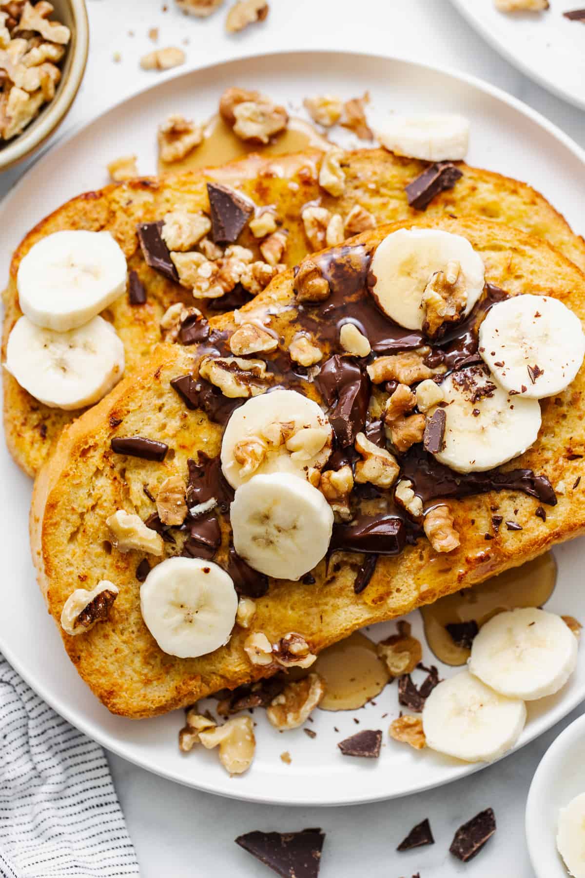 This air fryer chunky monkey French toast is a sweet breakfast eater's dream! The bread gets soaked in an egg mixture of banana, maple syrup, cinnamon, and peanut butter for an ultra-rich French toast topped with chocolate, roasted walnuts, and sliced bananas. Air fryer chunky monkey french toast in a plate.