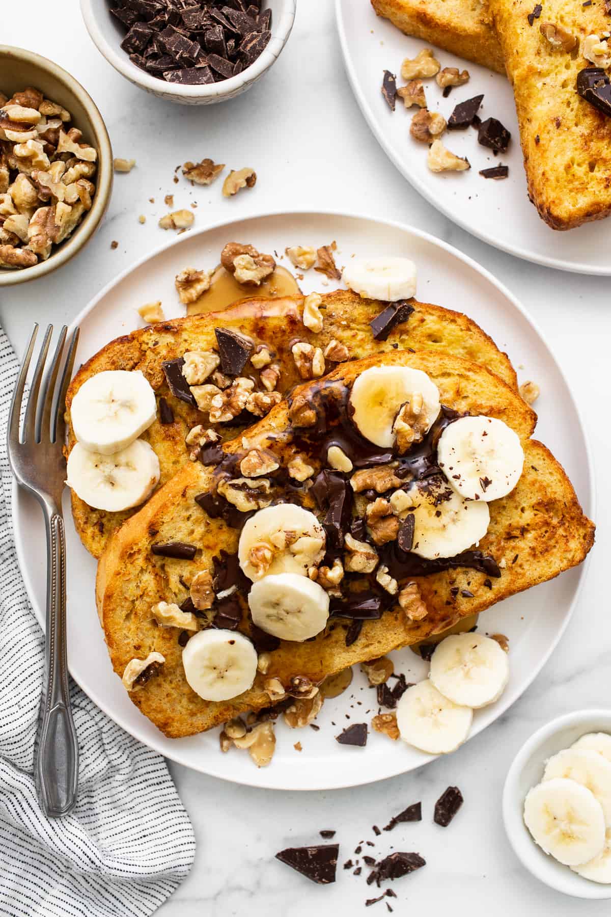 This air fryer chunky monkey French toast is a sweet breakfast eater's dream! The bread gets soaked in an egg mixture of banana, maple syrup, cinnamon, and peanut butter for an ultra-rich French toast topped with chocolate, roasted walnuts, and sliced bananas. Air fryer chunky monkey french toast on a plate.