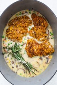Chicken breasts in a pan with mushrooms and sprigs of rosemary.