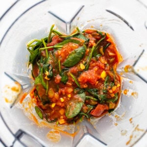 A blender filled with tomato sauce and spinach.
