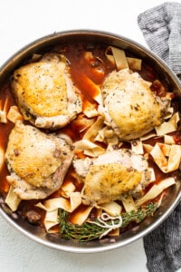 Chicken breasts in a pan with sauce and noodles.