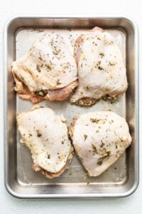 Chicken breasts on a baking sheet with herbs.