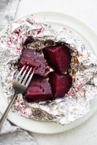 Beets in foil on a plate with a fork.