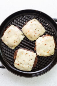 Four cheeseburgers in a grill pan on a white background.