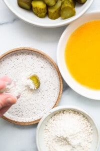A person is sprinkling flour on a bowl of pickles.