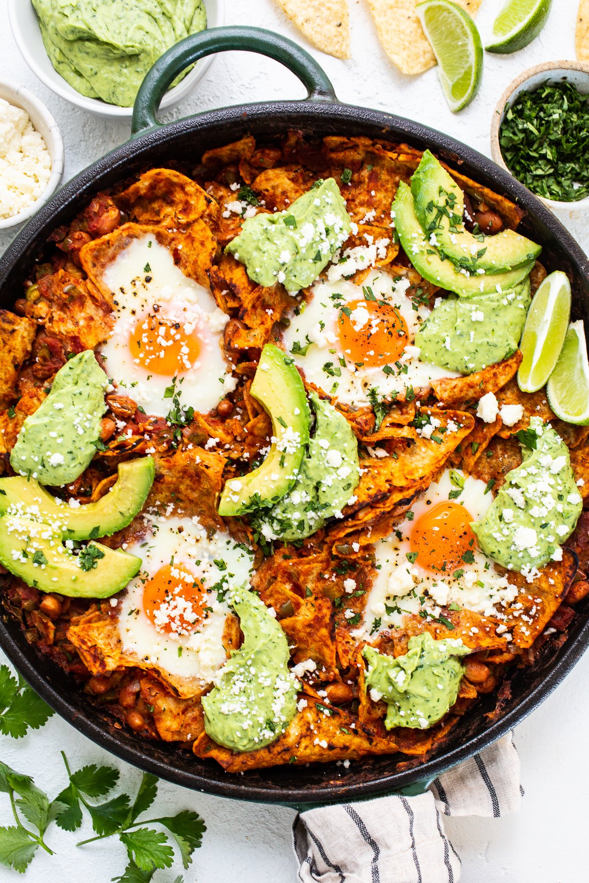 Learn how to make chilaquiles with this super simple chilaquiles recipe made with tomato sauce, spices, beans, tortilla chips, and baked eggs. chilaquiles with avocado crema in cast iron skillet.