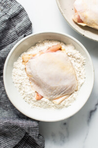 a white bowl filled with flour next to a chicken breast.