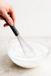 A person whisking milk in a glass bowl.