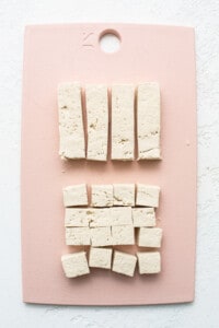 Tofu cubes on a pink cutting board.