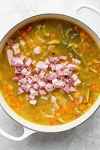 A pot of soup with ham and carrots.