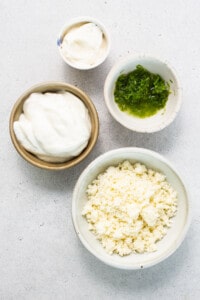 Three bowls of cheese, yogurt, and chives on a white surface.