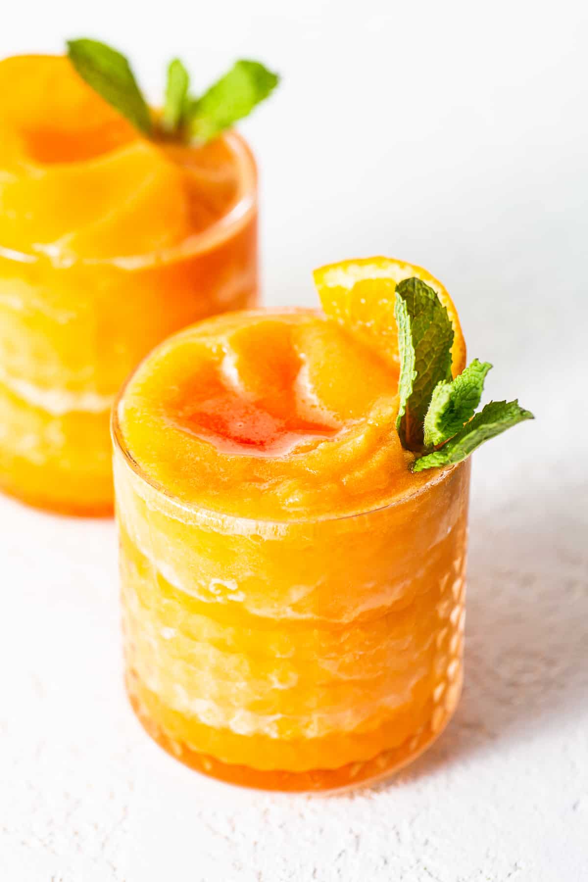 Frozen Aperol Spritz Slushies are the drink of the summer. Use frozen clementines to make it extra slushy and don't forget the Aperol and champagne. slushy in glass.
