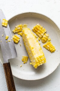 Corn on the cob on a plate with a knife.