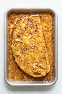 A slice of french toast in a pan on a white surface.