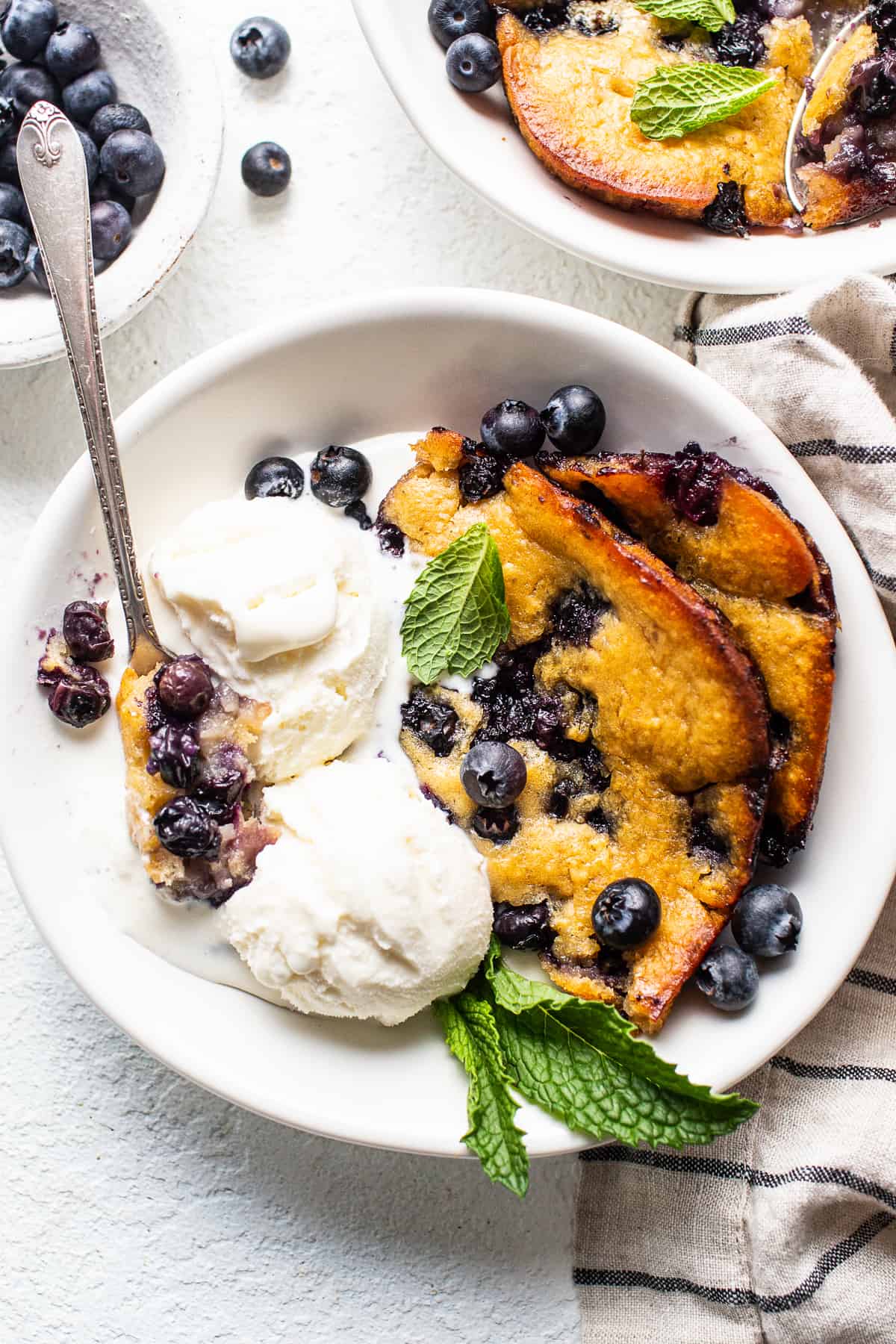 This stunning blueberry cobbler is made with bursting blueberries and a simple cobbler topping for a perfect summer treat. blueberry cobbler with ice cream in bowl.