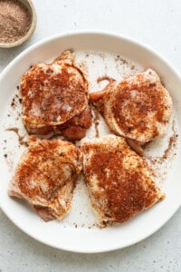 Four chicken breasts on a white plate with spices.