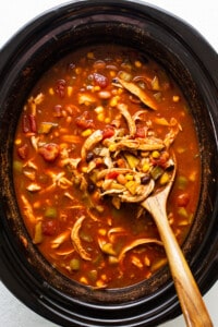 A bowl of chicken soup in a slow cooker with a wooden spoon.