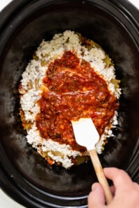a person stirring a mixture of food in a crock pot.