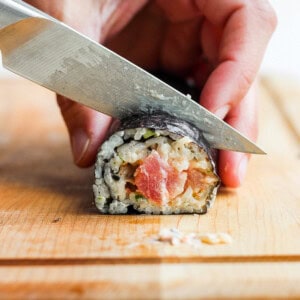 a person cutting sushi with a knife on a cutting board.