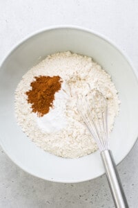 a bowl with flour, cinnamon, and a whisk.
