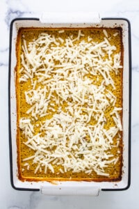A white baking dish with a layer of cheese on top.