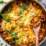 Chicken enchilada casserole in a pan with a wooden spoon.