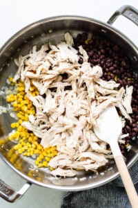 Chicken and corn in a pan with a wooden spoon.
