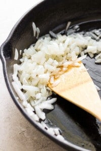 A frying pan with onions and a wooden spoon.