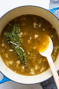 A pot of soup with a spoon and a sprig of thyme.