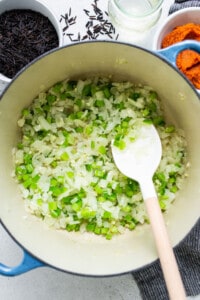 A pot full of onions and spices with a wooden spoon.