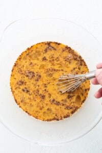 A person using a whisk to stir a cake on a plate.