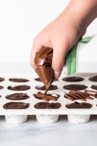 A person is dipping chocolate into a tray of cupcakes.