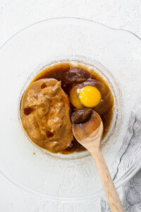 An egg in a glass bowl with a wooden spoon.