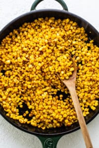 Corn in a skillet with a wooden spoon.