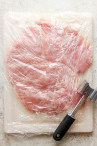 A piece of meat wrapped in plastic on a cutting board.