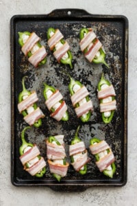 Bacon wrapped peppers on a baking sheet.
