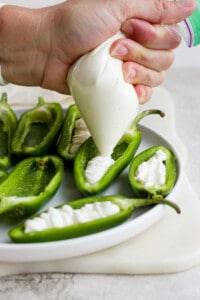 A person drizzling cream on green peppers on a plate.