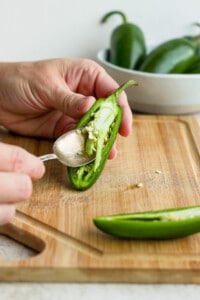 A person cutting a jalapeno pepper with a spoon.