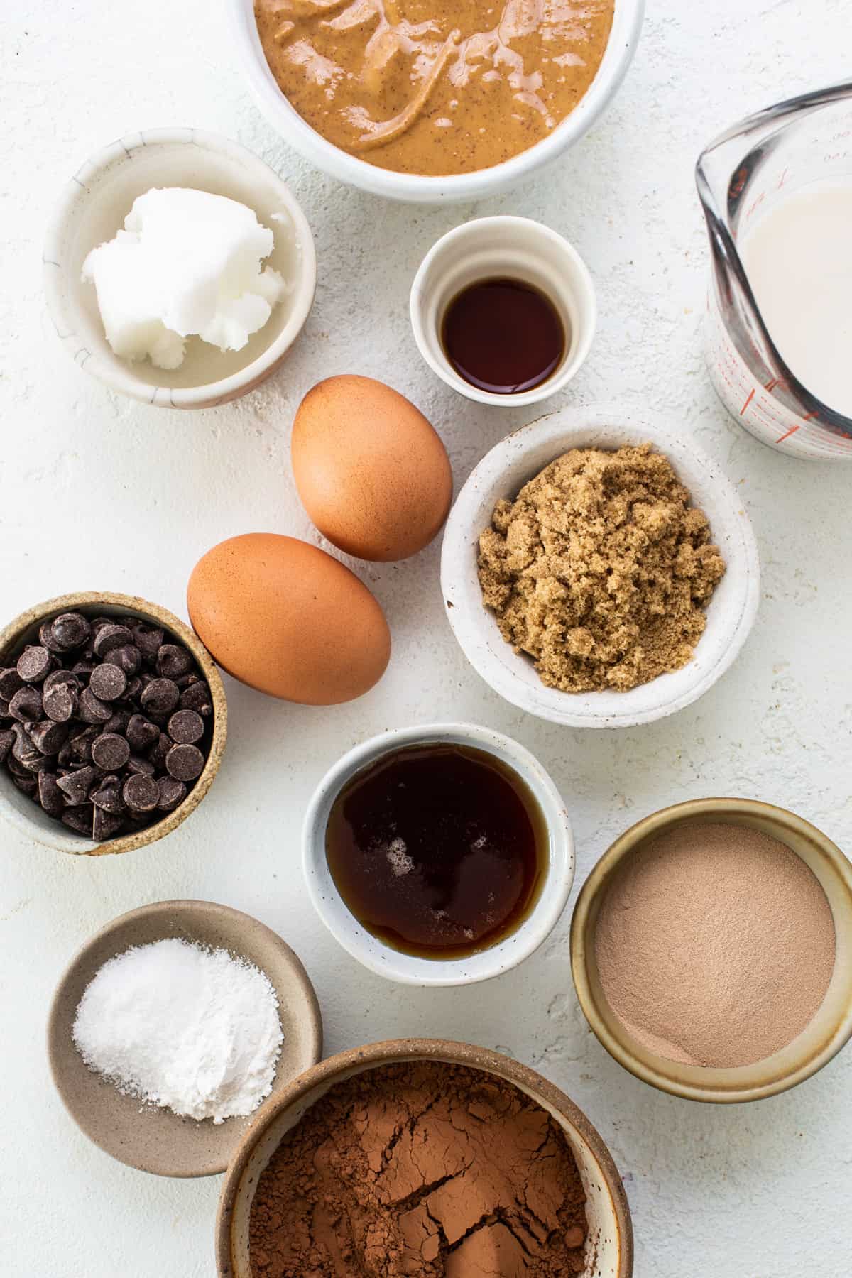 The ingredients for a chocolate cake are shown in bowls on a white background.