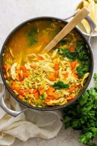 Chicken noodle soup in a pan with carrots and parsley.